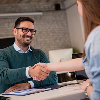 Dental patient shaking hands with team member at reception desk