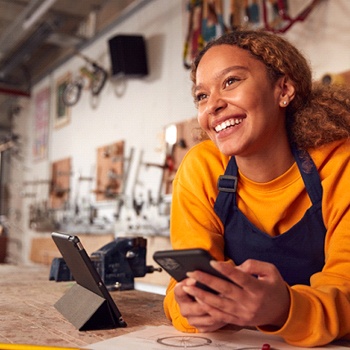 a shop owner leaning across a counter and smiling with a phone in their hands