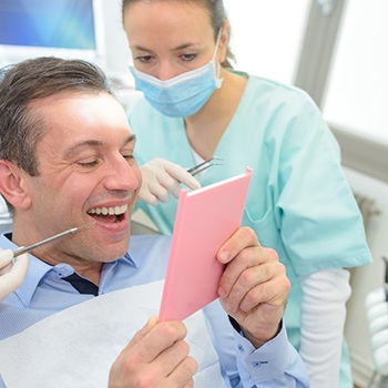 Man and dentist looking a this teeth in handheld mirror