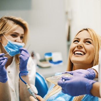 Woman in dental chair for emergency dentistry smiling at dentist