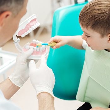 Dentist showing child how to brush teeth during children's dentistry visit