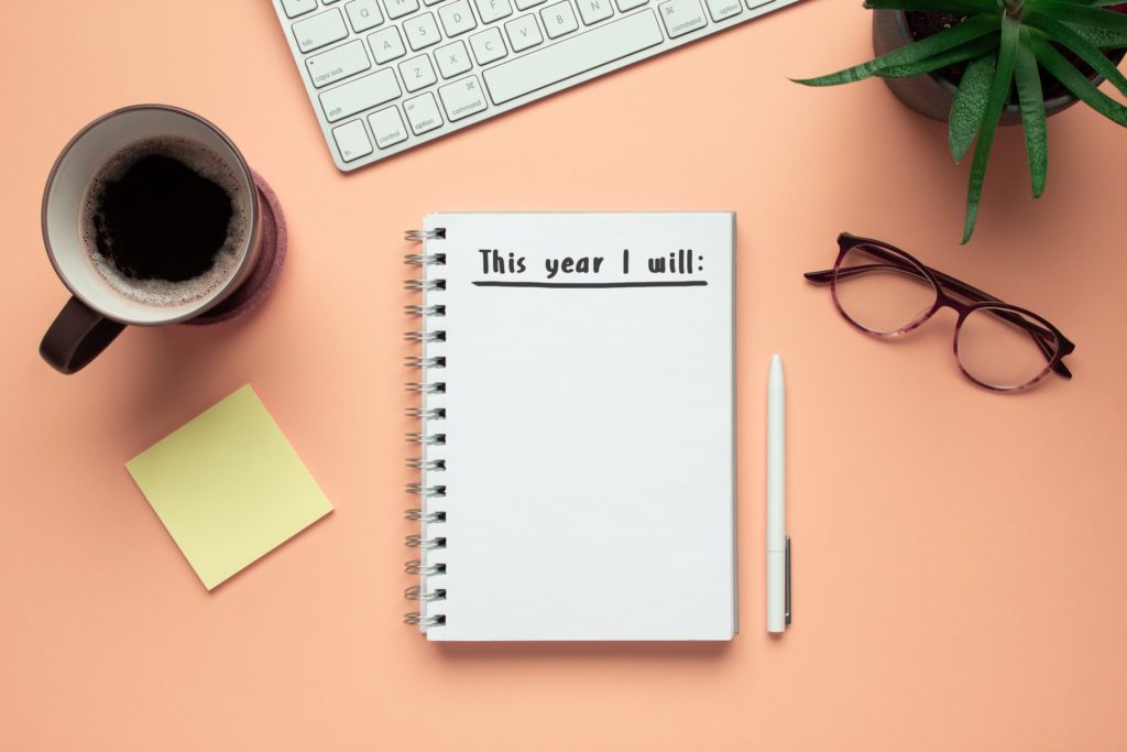 Notepad on desk with coffee, glasses, plant, and keyboard