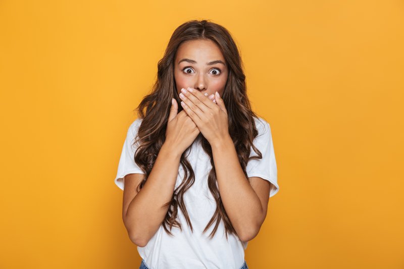A surprised woman covering her mouth against an orange background.