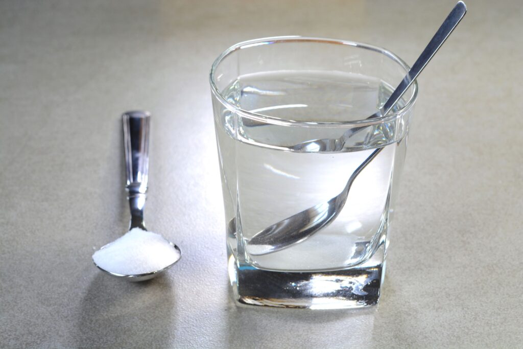 Clear glass of water with spoon next to spoonful of salt on countertop